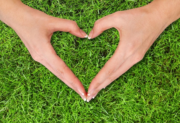 Young woman hands make heart symbol on green grass background