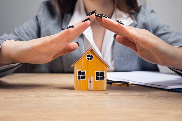 Young woman hands protecting a model of house on table