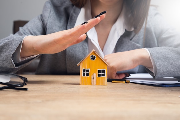 Young woman hands protecting a model of house on table