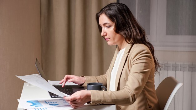 Young woman hands type on grey laptop keyboard and looks at graphs