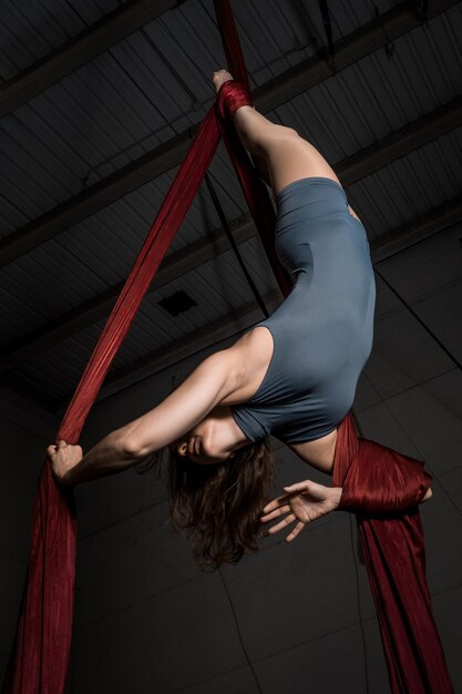 Photo young woman hanging on fabric while dancing against black background