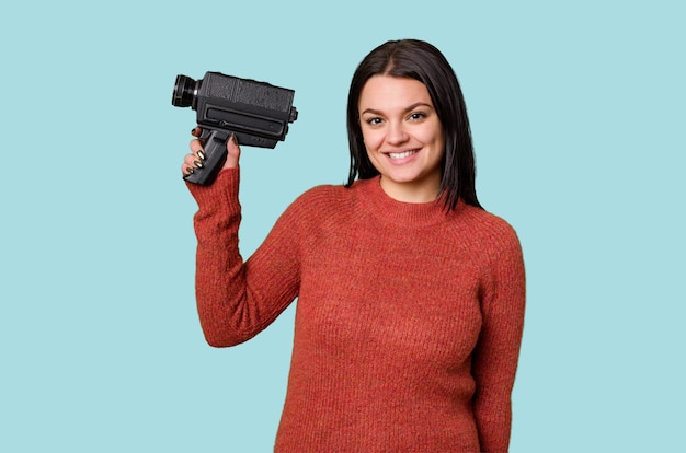 A young woman happily films with an antique video camera on an isolated background