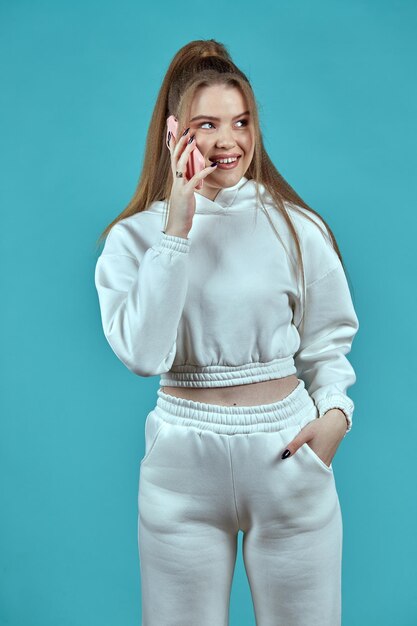 Фото Молодая женщина счастлива разговаривает по телефону, стоя на синем фоне