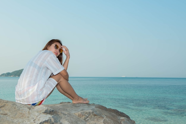 Young woman happy sitting on the rock at the beach