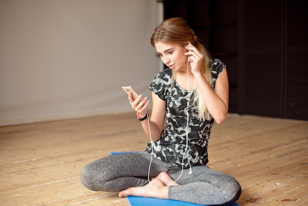 写真 幸せな若い女性は、電話で床に座って音楽を聴きながら、selfieを取ります。