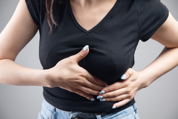 A young woman has a chest pain on a gray background