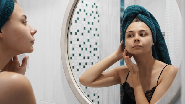 Young woman has problems with skin on the face - She looks in the mirror in the bathroom