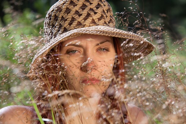 Giovane donna con un cappello tra l'erba illuminata dai raggi del sole su uno sfondo di foresta