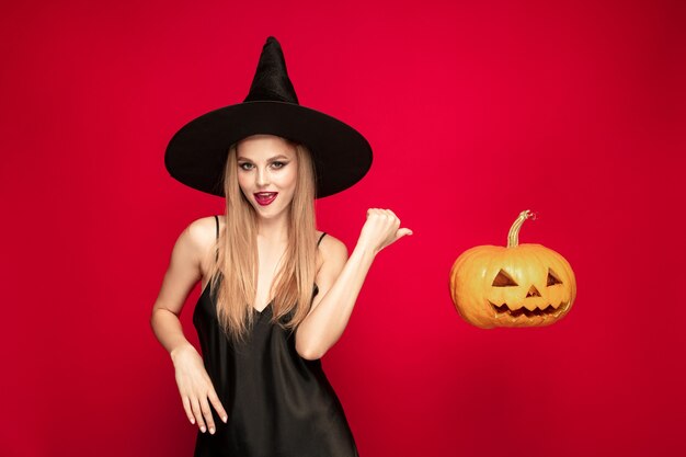 Young woman in hat as a witch on red background