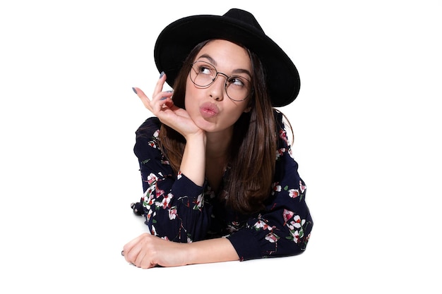 A young woman in a hat is lying on a white background Stylish model posing in the studio