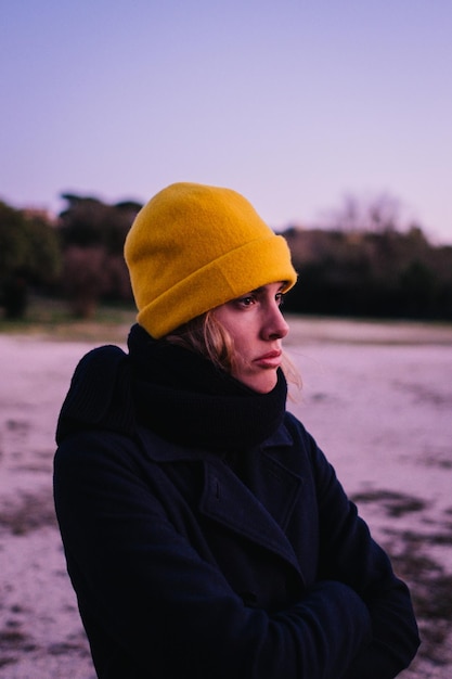 young woman in hat looking away while standing against sky during winter