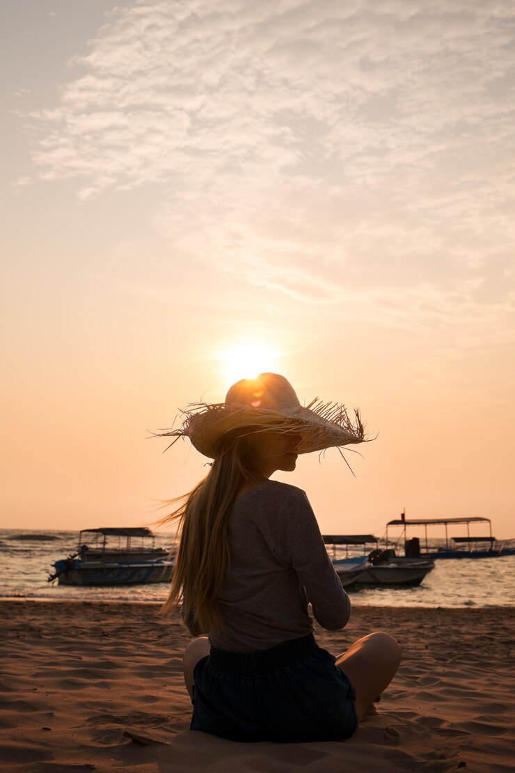 海に沈む夕日を眺める帽子をかぶった若い女性