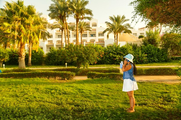 A young woman in a hat among palm trees speaks on the phone