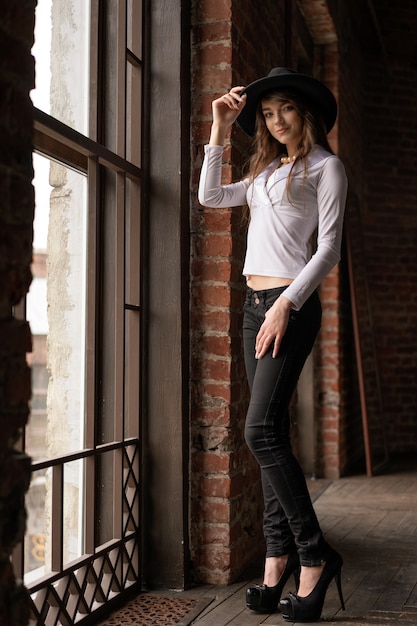 A young woman in a hat standing at the window, posing for the camera