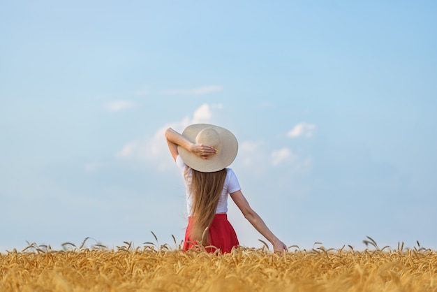 Young woman in hat stands in wheat field on blue sky background. Weekend outdoors