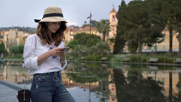 Young woman in hat typing in a phone background of Nice ancient buildings