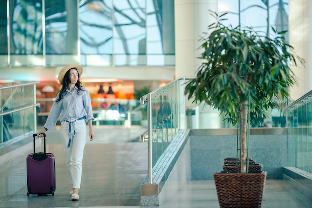 Молодая женщина в шляпе с багажом в международном аэропорту.