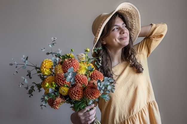 灰色の背景に菊の花束と帽子の若い女性