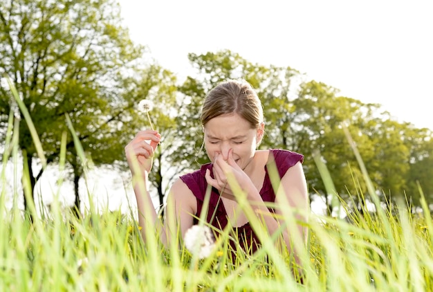 Foto giovane donna con una reazione allergica che tiene un dente di leone seduta contro gli alberi