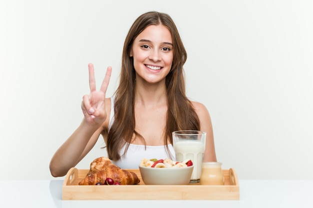 Young woman having breakfast showing number two with fingers