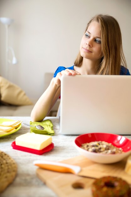 ラップトップコンピューターを使用しながら朝食をとっている若い女性。