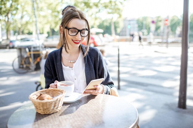 Young woman having a breakfast with coffee and croissant sitting outdoors at the french cafe in Lyon city