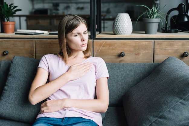 Young woman having chest pain sitting on sofa at home