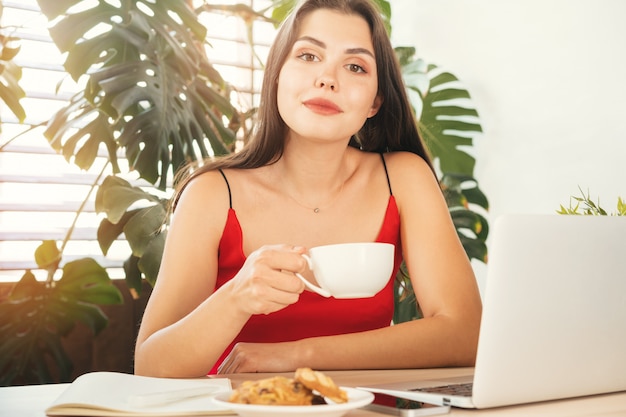 彼女のオフィスに座ってコーヒーブレークを持つ若い女性