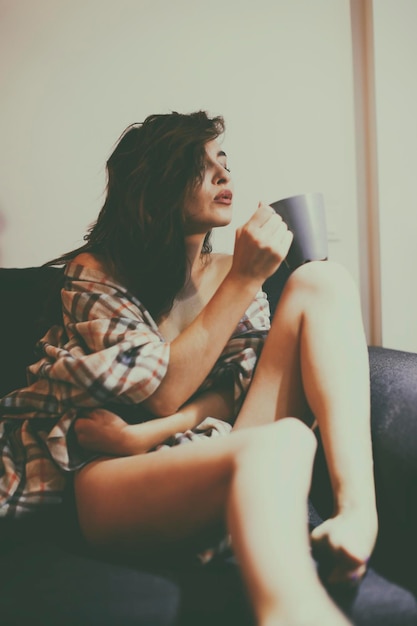 家のソファに座ってコーヒーを飲んでいる若い女性