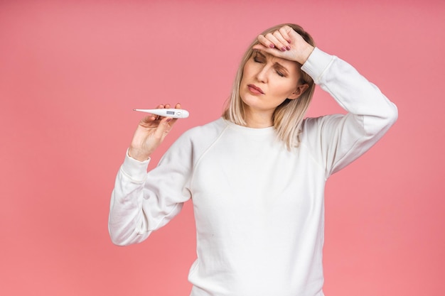 Young woman having flu taking thermometer. Isolated over pink background. Beautiful young woman is sick with a high temperature, a thermometer, isolated close-up. Cold, flu concept.