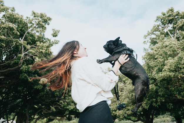 公園の肖像画のイメージで彼女の犬のフレンチ ブルドッグと遊んで踊って楽しんでいる若い女性 ペットの概念 家族の新しいメンバー 晴れた日に彼の犬を散歩に連れて行く女性