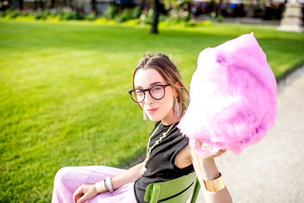 Foto giovane donna che si diverte con zucchero filato rosa seduto all'aperto al parco