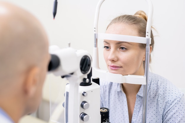 Foto giovane donna che ha la sua vista controllata da speciali apparecchiature optometriche in cliniche o in ospedale