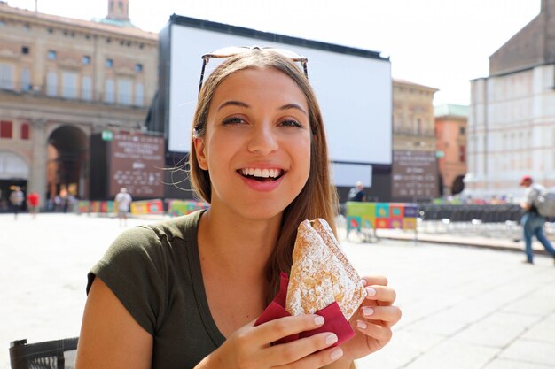 Young woman having italian breakfast with croissant and coffee at the cafe on the street in summertime