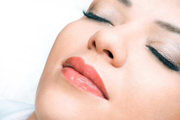 Young woman having permanent makeup on her lips at the beautician salon. Applying liquid glass to lips