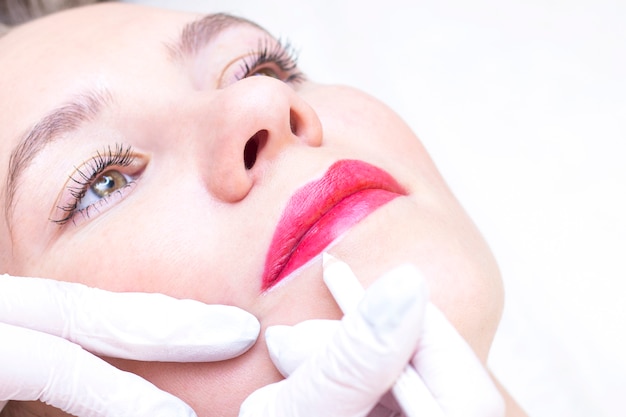 Young woman having permanent makeup on her lips at the beauticians salon. Permanent Makeup (Tattoo). drawing a contour with a white lip pencil