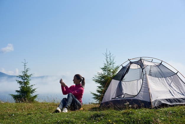 Giovane donna che ha un periodo di riposo vicino alla tenda turistica nella mattina d'estate in montagna