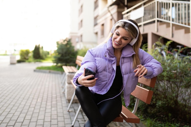 Young woman in headphones speaks by video link sitting next to an apartment building