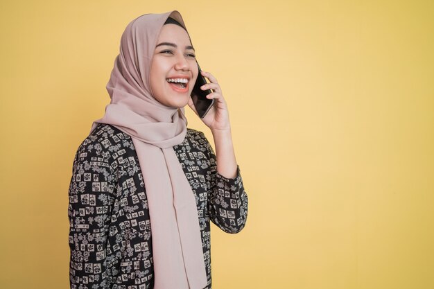 Young woman in headscarf smiling broadly while getting a call with happy gesture with copyspace