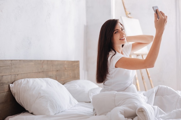 Young woman of a heavenly beauty looking fantastic while taking a morning selfie in bed