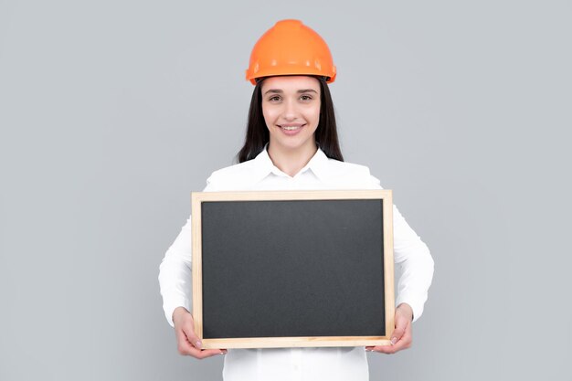 Young woman in helmet hold board on gray background Architect businesswoman in helmet thinking young caucasian female in work as constructor engineer