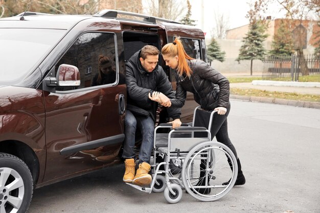 Young woman helping handicapped man to sit in wheelchair