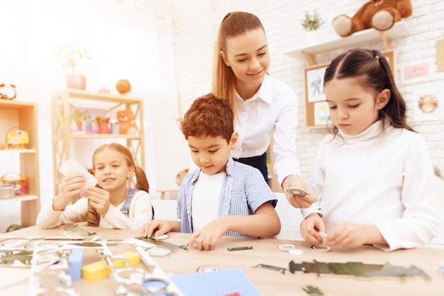 A young woman helps children fold parts from cardboard.