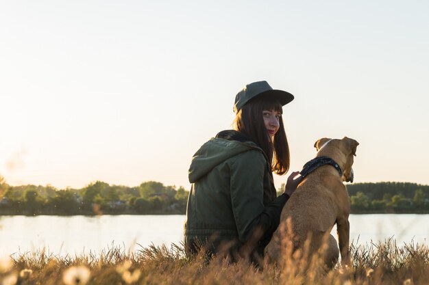 Young woman and her dog by the lake at sunset