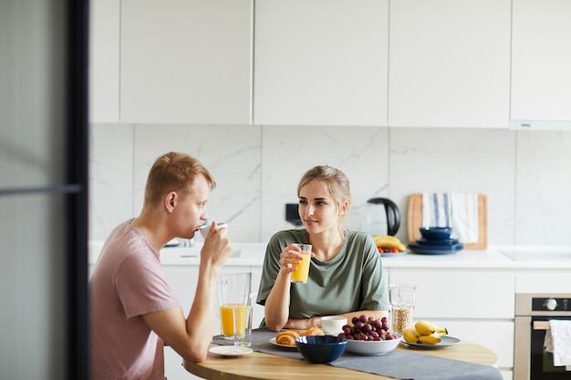 Young woman and her husband drinking orange juice by breakfast