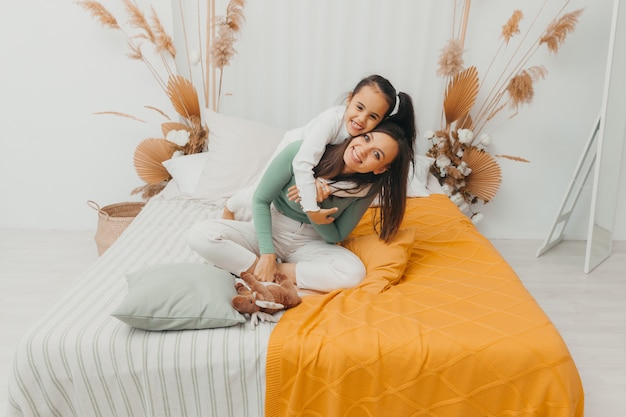 Young woman and her little daughter are having fun in bed at home. A happy family.