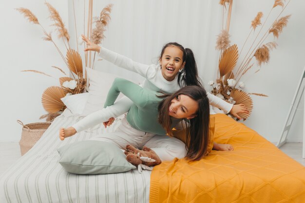 Young woman and her little daughter are having fun in bed at home. A happy family.