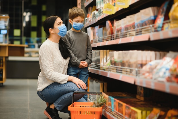 젊은 여자와 그녀의 작은 아들 입고 보호 얼굴 마스크는 슈퍼마켓에서 음식을 쇼핑