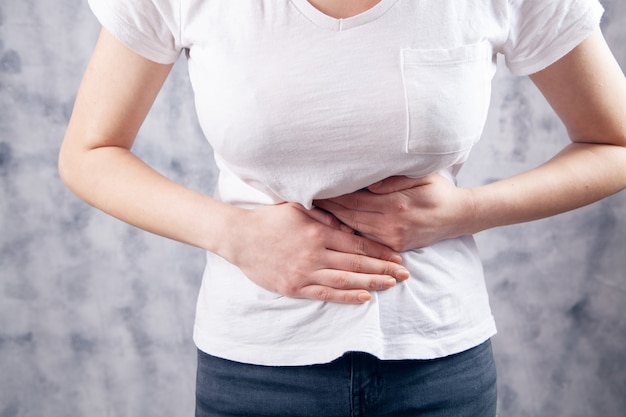 In a young woman, her stomach hurts on a gray background