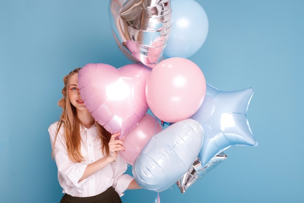 Young woman hid behind balloons on a blue surface